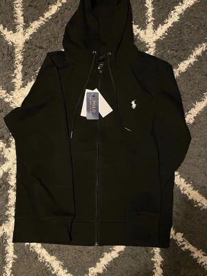 Svart hoodie från Polo Ralph Lauren - Snygg svart hoodie med dragkedja från Polo Ralph Lauren. Helt ny och pris kan diskuteras därför tar jag gärna emot prisförslag 