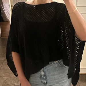 Svart virkad poncho / poncho topp i 50% bomull - Snygg, svart hålmönstrad poncho i luftig modell – tillverkad i Italien! Perfekt att slänga över ett linne för en stilren och avslappnad boho-look. Passar även som cover up till stranden.   Storlek ONESIZE, passar i princip alla med XS-XL (jag har vanligtvis S).  Nyskick 