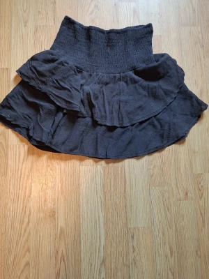 Super söt svart volangkjol - Kort svart kjol med bred smock i midjan och dubbla volanger. Kjolen har en luftig och flowy känsla, perfekt för dig som gillar en avslappnad men ändå söt stil. Materialet känns mjukt och lätt, vilket gör den bekväm att bära.💗 