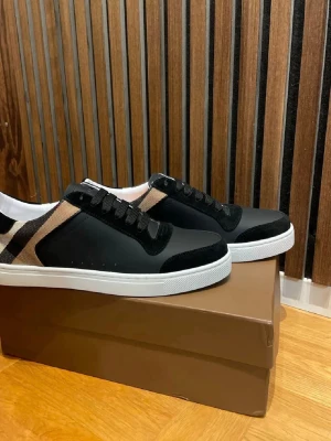 Burberry skor  - Snygga sneakers i svart med klassiskt beige, svart och vitt rutmönster på sidorna. Skorna har svarta snören, vit sula och detaljer i mocka och textil. Perfekta för dig som vill ha en stilren men ändå unik look. Stl 45 väldigt snygga och oanvända 