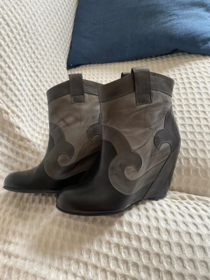 Gråa wedge cowboy boots - Bianco Cowboy boots i grått och svart med kilklack. Väldigt fint skick men har tyvärr blivit för små. Står 39 i storlek men skulle säga att de är små i storleken så borde passa en 38 perfekt