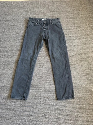 Grå Jack & Jones - Passar 34/34. Säljer ett par grå loose fit jeans från Jack & Jones. Klassisk femficksmodell med raka ben och bälteshällor. Jeansen har en avslappnad passform och är tillverkade i denim. Perfekta för en chill och stilren look.