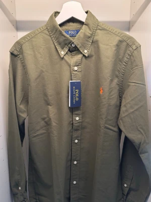 Ralph Lauren Skjorta - Säljer en grymt sjyst Ralph Lauren skjorta i en fin grön färg med passande orange ”häst”. Köpt på Volt för 1795 kr. Skjortan är helt ny med prislapp kvar. KAN GÅ NER I PRIS VID SNABB AFFÄR! ™️