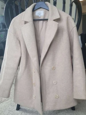 AFJ x NA-KD beige kavaj, storlek 34 - En dubbelknäppt kavaj med slagkrage och knappar framtill. Kavajen har en rak passform och långa ärmar.