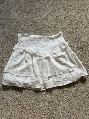 Vit volangkjol från Gina Tricot - Supersöt vit kortkjol från Gina Tricot med bred smock i midjan och dubbla volanger. 