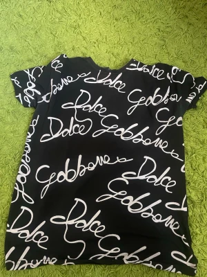 Dolce & Gabbana  - Snygg svart t-shirt med vit, handskriven textprint dolce & Gabbana över hela framsidan. T-shirten har klassisk passform och korta ärmar. Perfekt för dig som gillar statement-plagg och vill sticka ut lite extra.