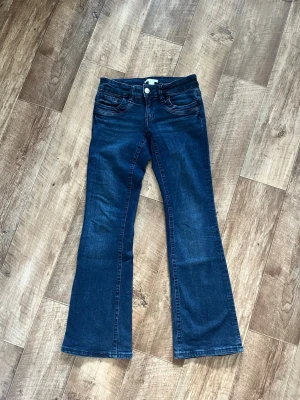 Mörkblå bootcut jeans Gina Tricot - Snygga mörkblå bootcut jeans från Gina Tricot i klassisk femficksmodell. Jeansen har utsvängda ben och låg midja. Tillverkade i mjukt denimtyg med lite stretch för extra komfort. Perfekta för en trendig och avslappnad stil.