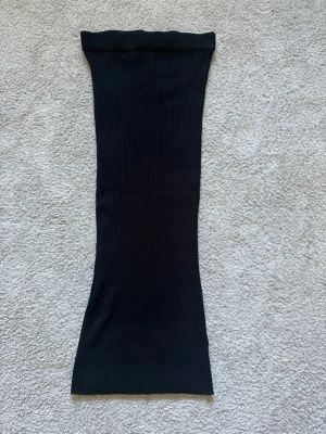 Svart ribbad långkjol - Svart ribbad långkjol med stretchig passform. Kjolen har en enkel och stilren design med raka linjer och är perfekt för dig som gillar minimalistisk stil. Materialet känns mjukt och följsamt mot kroppen.