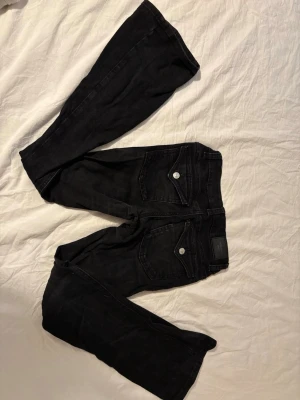 Svarta Perfect Jeans från Gina Tricot - Säljer ett par svarta Perfect Jeans från Gina Tricot. Jeansen har smal passform, klassiska bakfickor med silverknappar och bälteshällor. Materialet är stretchigt och bekvämt, perfekt för en trendig och avslappnad look.