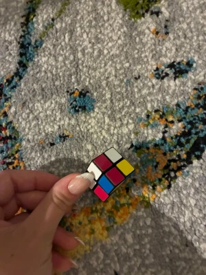 Mini Rubiks kub - En liten Rubiks kub i miniformat, perfekt som dekoration. Kuben har färgerna röd, vit, gul, grön, rosa och blå och är gjord av plast. Smidig att ha med sig och rolig att lösa när man har tråkigt.
