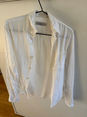 Vit skjorta från Dries Van Noten - Klassisk vit skjorta från Dries Van Noten med krage och knappar framtill. Skjortan har lång ärm och är tillverkad i ett lätt och luftigt material, perfekt för en stilren look. Passar till många olika outfits och är enkel att matcha.