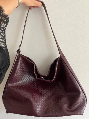 Vinröd axelväska med flätad look - Stilren vinröd axelväska i konstläder med flätad struktur och justerbart axelband. Den stängs med magnetknapp. Rymlig och passar perfekt som skolväska❣️