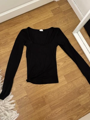 Svart långärmad topp Gina Tricot - Svart långärmad topp från Gina Tricot med fyrkantig ringning. Tillverkad i mjukt och stretchigt material som sitter snyggt på kroppen. Perfekt att styla med jeans eller kjol för en clean look. *sista bilderna är samma tröja i marinblått*