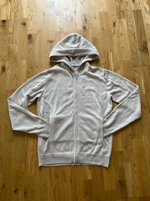 Beige kashmere zip från RYVLS - Snygg beige kashmere zip från RYVLS i mjukt och tunt material. Modellen har dragkedja framtill, två fickor och en klassisk huva. Perfekt för dig som gillar en clean och enkel stil. Passar till det mesta och är superenkel att matcha med andra plagg. Nypris på kidsbrandstore ca 1300 mitt pris 999. HELT OANVÄND! STORLEK 170-176 men PASSAR BÅDE OM DU ÄR LÄNGRE ELLER KORTARE! Pris ej hugget i sten och öppen för byten!