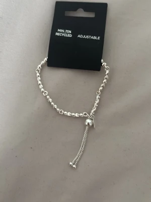 Silvrigt justerbart pärlarmband pilgrim - Snyggt armband i silverfärg med små pärlor längs hela bandet. Armbandet är justerbart med en glidande låsdetalj och två tunna kedjor som avslut helt nytt och oanvänt 