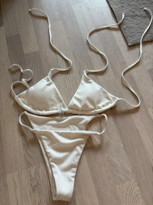 Vit ribbad bikini med knytband - endast testad  - Snygg vit bikini med ribbad struktur och smala knytband både upptill och nedtill. Klassisk trekantsmodell på toppen och högt skurna trosor. Perfekt för strandhäng eller poolparty i sommar! Endast testad storlek M