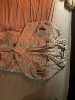 Unik Grå Stickad Tröja - Stickad hoodie med dragkedja framtill,  bröstfickor med knappar och ribbade muddar. Perfekt nu inför hösten!