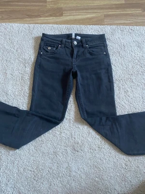Svarta skinny jeans med silverknappar från H&M - Snygga svarta skinny jeans med fem fickor och silverfärgade knappar både fram och på bakfickorna. Jeansen har en klassisk midja och smal passform hela vägen ner. Perfekta till en avslappnad eller trendig look.