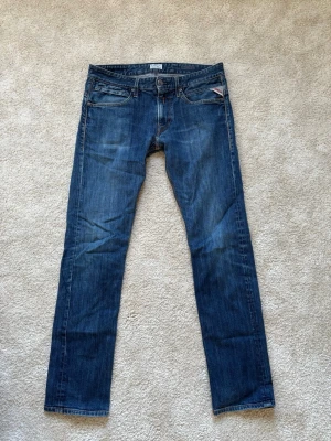  replay jeans  - Säljer ett par blå jeans med rak passform. Jeansen har en mörk tvätt med subtila slitningar och kontrastsömmar. Materialet är denim i bomull och de har normal midja. Perfekta för en avslappnad och stilren look.