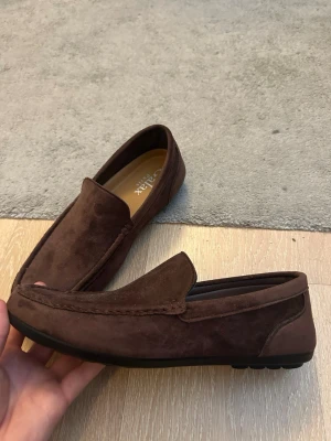 Bruna mockaloafers från Galax Paris - (Använda MAX 3 gånger efter att jag köpte dem i Spanien för något år sedan, !Inga defekter alls!).                                                                     Snygga bruna loafers i mocka från Galax Paris. Skorna har en klassisk, stilren design med rundad tå och diskreta sömmar. Yttermaterialet är mjukt mockaskinn och sulan är svart och greppvänlig. Perfekta för dig som gillar en clean och tidlös look.