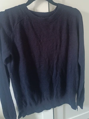 Mörkblå enkel stickad tröja - Mörkblå stickad tröja med rund halsringning och långa ärmar. Tröjan har ribbade muddar vid ärmslut och nederkant. Materialet ser mjukt och bekvämt ut, perfekt för kyligare dagar.