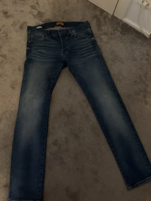 Jack and Jones jeans - Snygga blå slim fit jeans med klassisk femficksdesign och tvättade detaljer på låren. Jeansen har normal midja och raka ben, perfekta till en avslappnad stil. Materialet är denim i bomull med lite stretch för extra komfort.