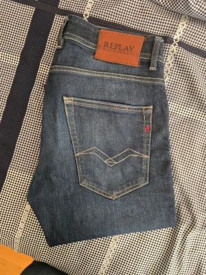 Mörkblå jeans från Replay - Snygga mörkblå jeans från Replay med klassisk femficksmodell och kontrastsömmar. Jeansen har en skinnpatch med logga bak i midjan och diskreta slitningar framtill. Tillverkade i slitstarkt denimtyg, perfekta för en trendig vardagslook.
