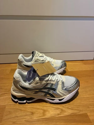 Asics Gel-Kayano 14 sneakers  - Snygga sneakers från Asics i vitt och silver med mesh- och syntetpaneler. Skorna har en sportig design med svarta detaljer och klassisk Asics-logga på sidan. Lågt skaft och tjock sula för skön komfort. Perfekta för dig som gillar streetwear och sportig stil.