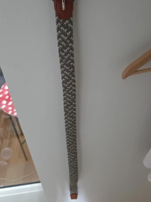 Flätat bälte från jack and jones - Snyggt flätat bälte i gråa och beige toner med detaljer i brunt läder. Perfekt accessoar för att lyfta din outfit med en stilren och modern touch. Bältet har en flexibel vävd design som gör det bekvämt att bära och lätt att justera.