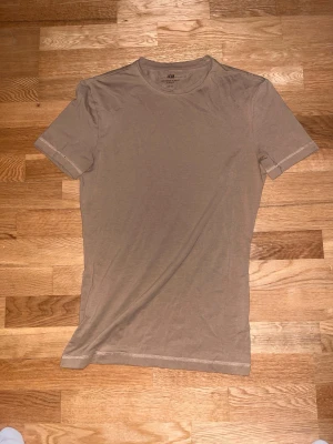 Beige slim fit t-shirt från H&M - Snygg beige t-shirt från H&M i slim fit-modell. T-shirten har rund halsringning och korta ärmar, tillverkad i mjuk bomull som känns skön mot huden. Perfekt basplagg för alla tillfällen och enkel att matcha med olika stilar.