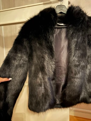 Svart fluffig pälsjacka - Snygg svart pälsjacka. Perfekt för dig som vill ha en trendig och varm look under kalla dagar. Kan stängas framtill och har en mjuk, lyxig känsla.