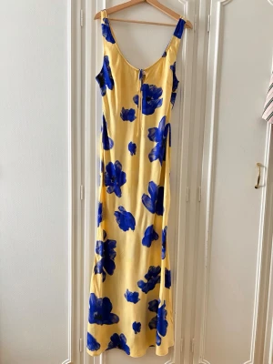 Gul långklänning med blå blommor - Gul långklänning med stora blå blommor från Asos. Klänningen har ärmlös design, djup urringning och knytband framtill. Materialet är lätt och mjukt. Helt oanvänd med alla lappar kvar på! Nypris är 369 kr. 