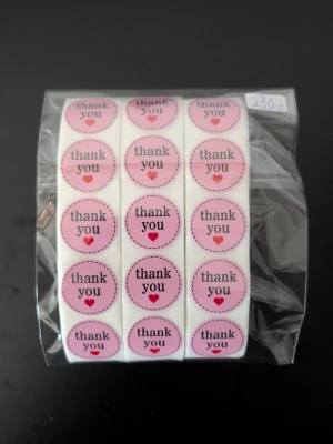 Rosa thank you-klistermärken 230 st - Ett ark med runda klistermärken i rosa nyanser med texten 'thank you' och ett litet rött hjärta. Perfekt för paket, brev eller presenter. Klistermärkena är förpackade i en genomskinlig plastpåse.