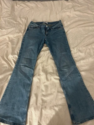 Blå bootcut jeans med låg midja - Säljer ett par klassiska blå bootcut jeans med låg midja och fem fickor. Jeansen har en lätt tvättad look och vida ben från knät och ner. Perfekta för dig som gillar retrostil och vill ha ett par bekväma jeans i bomull. Säljer pågrund utav att de inte passar mig och nästan aldrig kommer till användning 