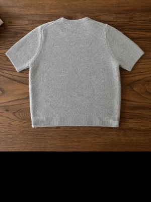 Ljusgrå kortärmad tröja från Zara - En stilren ljusgrå tröja från Zara med korta ärmar och rund hals. Tröjan är stickad i ett mjukt material och har ribbade kanter vid ärmslut, halsringning och nederkant. Perfekt för en clean och enkel look.