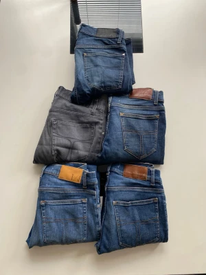 Fem par jeans i olika blå nyanser - Säljer fem par jeans i olika blå tvättar och ett par i grått. Klassisk femficksmodell med raka ben och bälteshällor. Några har läderpatch bak i midjan. Perfekta för dig som vill ha flera stilar att variera mellan.