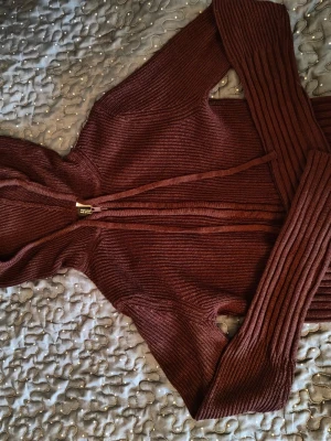Mörkröd ribbad hoodie med dragkedja - Säljer en vinröd hoodie med ribbad struktur och dragkedja framtill. Tröjan har huva med snören och långa ärmar med breda muddar. Materialet är stickat . Jag säljer den för att jag inte gillar hur den sitter på min passform, fast jag älskar färgen😞