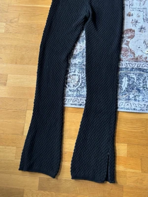 Axel Arigato Svarta leggings med struktur och slits - Axel Arigato storlek M                Säljer ett par svarta leggings med coolt 3D-strukturmönster. De har utsvängda ben och en liten slits längst ner vid benslutet. Materialet är stretchigt och mjukt, perfekt för en trendig och bekväm look. Nyskick, oanvända