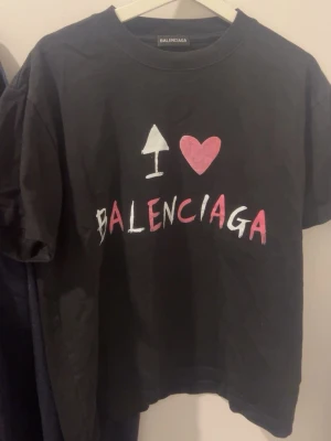Svart Balenciaga t-shirt med tryck - Cool svart t-shirt från Balenciaga med trycket 'I ❤️ BALENCIAGA' i vitt och rosa på bröstet. Klassisk rund hals och korta ärmar. Tillverkad i mjuk bomull för en skön känsla och avslappnad passform.