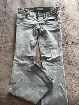 Ljusgrå bootcut jeans - Säljer ett par ljusgrå jeans med bootcut och klassisk femficksmodell. Jeansen har snygga sömmar på bakfickorna och är tillverkade i ett mjukt denimtyg. Passar perfekt till en avslappnad stil och är lätta att matcha med olika plagg. Det är low waist väldigt låga i midjan! Använda två gånger. 