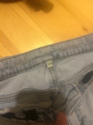 Ljusblå raka jeans i storlek 164 - Säljer ett par ljusblå jeans med raka ben och klassiska bakfickor. Jeansen har hög midja och är tillverkade i ett mjukt denimtyg. Perfekta för en avslappnad och trendig look.