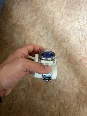 Stilren klocka med blå urtavla - Säljer en snygg klocka med blå urtavla och silverfärgat armband i metall. Klockan har en modern och stilren design med markerade timmarkeringar och robust länkarmband. Perfekt accessoar för dig som vill ha något klassiskt men ändå trendigt.