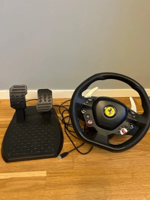 Thrustmaster t80 Ratt och pedaler Ferrari gaming - Säljer en svart racingratt med Ferrari-logga och tillhörande pedaler, perfekt för bilspel på konsol eller PC. Ratten har flera knappar, växelpaddlar i silver och ansluts via USB. Materialet är mestadels plast med detaljer i metall.