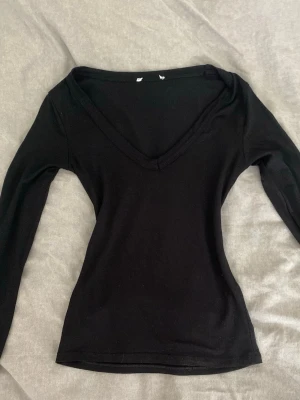 Svart långärmad v-ringad topp - En svart långärmad topp med v-ringning och figurnära passform. Perfekt basplagg som är lätt att matcha till olika outfits. Tillverkad i mjukt material som känns skönt mot huden.