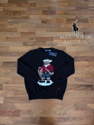 Ralph Lauren Stickad Bear Sweater - Säljer en helt ny Polo Ralph Lauren Polo Bear stickad tröja i storlek M. Oanvänd med originaltaggen kvar. Svart modell med den ikoniska Polo Bear framtill i röd outfit, detaljerade broderier och klassiska röda RL-initialer. Rund hals samt ribbstickade muddar vid hals, ärmar och nederkant. En exklusiv och tidlös tröja som passar perfekt till både vardag och finare outfits. Tagg acklippt. Inga fläckar, hål eller defekter. 📦 Snabb leverans – skickas samma dag (om ej hinder).