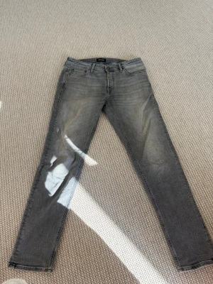 Grå slim fit jeans från Jack & Jones - Snygga grå slim fit jeans från Jack & Jones med klassisk femficksmodell och dragkedjegylf. Jeansen har en tvättad look och raka ben som sitter tajt. Perfekta till en avslappnad stil och passar till det mesta i garderoben.