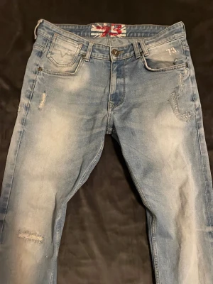 Pepe london jeans  - Säljer ett par ljusblå jeans med slitningar och tvättade detaljer. Jeansen har fem fickor, knappgylf och en snygg patch baktill i midjan. De har en avslappnad passform och är tillverkade i klassisk denim. Perfekta för en cool och avslappnad stil.