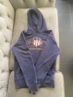 Marinblå Gant Hoodie Storlek S - GANT hoodie i marinblått. I bra skick och inga större defekter, men är lite sliten vid armbågarna, vilket syns på bilderna. Annars fint skick. Storlek S.