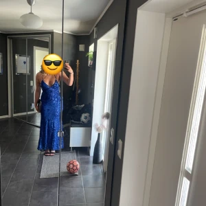 Balklänning - Blå balklänning med paljetter samt öppen rygg med snörning. Storlek S, jag är 173 cm för jämförelse. Pga knytningen i bak så kan man anpassa passformen.  Använd endast en gång.  