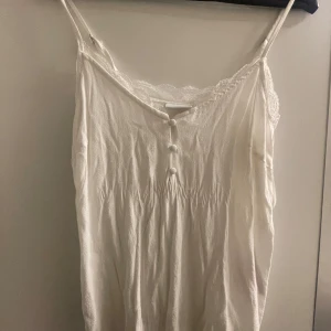Vit topp - Vit topp med knappar vid brösten samt spets vid kanterna längst upp. 